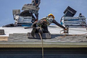 A roofer applying a light-colored, reflective coating to a residential sloped roof on a sunny day.