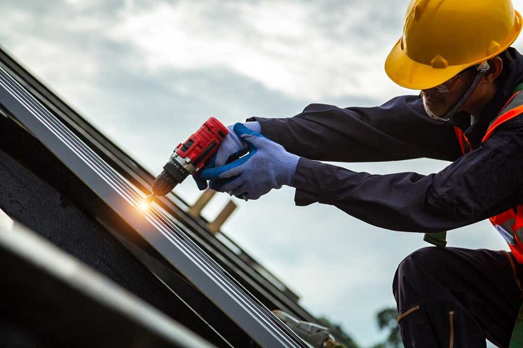 A homeowner in autumn removing leaves from a sloped roof using gloves and a gutter scoop.