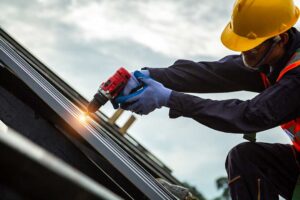 A homeowner in autumn removing leaves from a sloped roof using gloves and a gutter scoop.