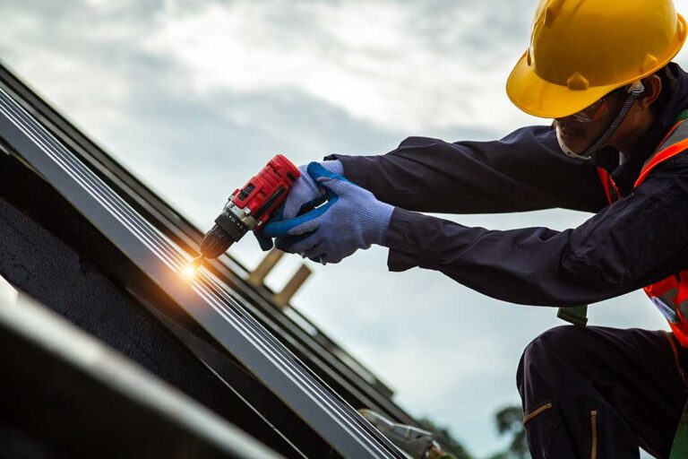 A homeowner in autumn removing leaves from a sloped roof using gloves and a gutter scoop.